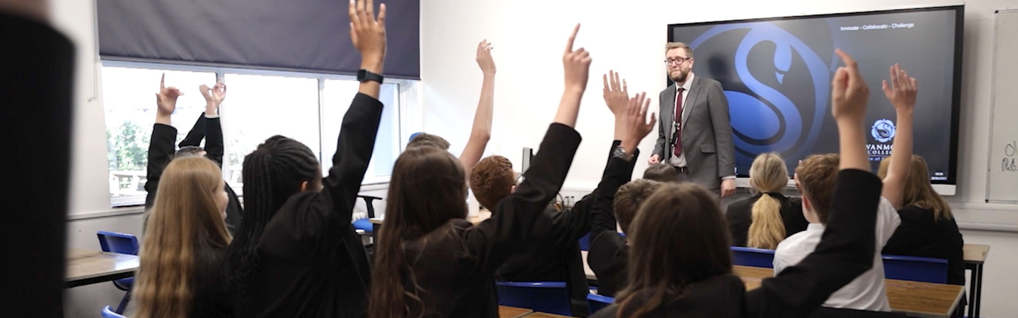 Image shows pupils putting their hands up in class.