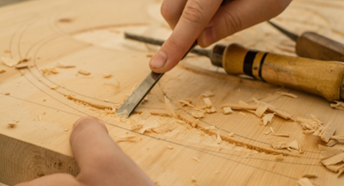 Image shows a person using a chisel to engrave a design onto wood