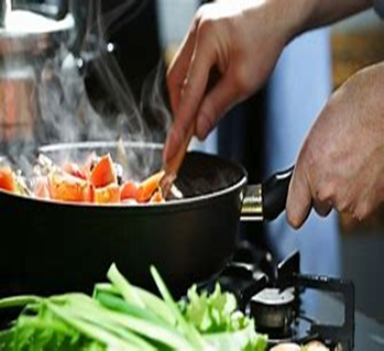 Image shows stirring vegetables in a saucepan on the hob, with a pile of greens next to it