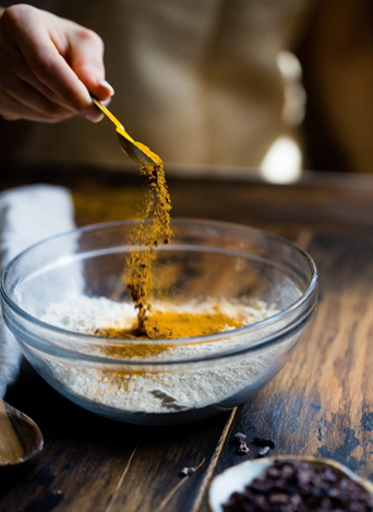 Image shows someone holding a small spoon sprinkling spices into a bowl of flour