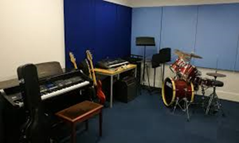 Image shows one of the Swanmore College Music classrooms with keyboards, guitars, electric guitars, and a drum kit