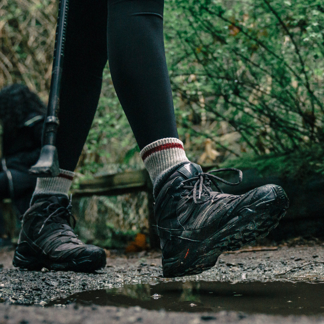 Image shows a close up of someone walking on a damp woodland path in walking boots