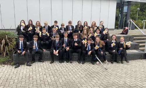Image shows a group of pupils sitting on the steps of the Performance Building celebrating their Kindness Awards and holding their Swan Cafe vouchers